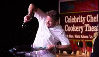 James Martin, celebrity chef performing some dynamic chef move with a teaspoon and frying pan.