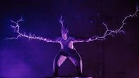 Wilderness festival performance photo showing person in chain-mail suit with electricity sparks coming out from head and hands.