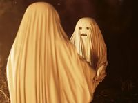 Still image from a short film, person covered by a sheet with eyes and mouth cut out to look like a ghost.