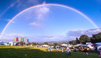 Underneath The Stars festival under a huge rainbow against a blue sky.