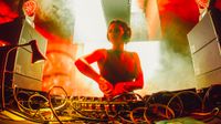 Woman DJ performing at Terminal V Festival, surrounded by vibrant lights and smoke, immersed in her music set.