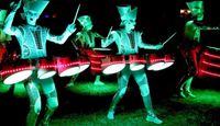 Drummers at Lindisfarne Festival, drums are filled with lights and performers are walking around in costume beating their drums.