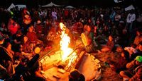Gathering around the Soul Revolution Festival fire, goers playing drums and adding wood to fire, festival crowd surrounding the space.