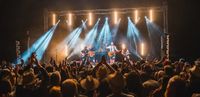 An energized crowd at Black Deer Festival enjoys a live music performance with artists on stage illuminated by dramatic stage lighting.