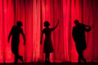 Silhouette of actors behind a red theatre curtain.