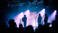Music performer playing on stage at Supersonic Festival, purple stage lights with crowd in shadows in foreground.
