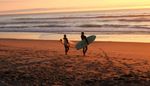 Surfers about to enter the sea at sunset.
