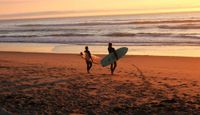 Surfers about to enter the sea at sunset.