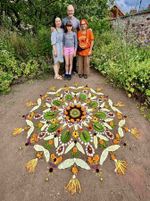 Four people standing behind a circular mandala made with flowers, leaves, stones and other natural materials; photograph by James Craig Page.