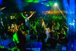 Band performing under green and blue stage lighting in front of an indoor audience.
