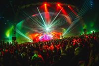 View of the Pavilion Festival main stage from inside a large crowd. The stage is filled with light and lasers.