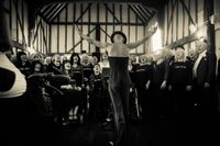 A choir singing together on stage in a Traditional UK barn, with choir master in front conducting.