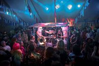 Musicians at Lindisfarne Festival under a small stage lit awning inside a marquee tent.
