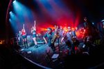 Singers and a brass section performing together beneath red and blue stage lighting. Photograph by Will Bailey Photography.