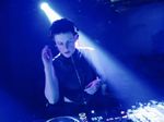 DJ wearing headphones while performing beneath blue stage lighting.