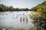 Festivalgoers swimming and paddling in the tree-lined lake at ALSO Festival.
