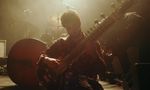 Seated musician playing a sitar under warm stage lighting.