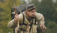 Man dressed in old military clothes holding a walking stick.