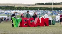 Festival goers standing behind a huge Vegan sign in a field with campsite in the background.