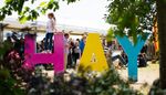 Young person climbing on the Hay Literary Festival sign with marquee in the background.