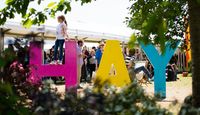 Young person climbing on the Hay Literary Festival sign with marquee in the background.