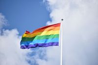 Rainbow flag against a blue and cloudy sky.