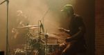 Drummer performing under warm stage lighting, with another musician behind the drum kit.