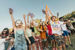 Children wearing handmade masks and raising their arms during an outdoor activity at ALSO Festival.