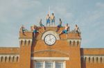 'Above & Beyond' performers in a symmetrical formation hanging off the side of the building with clock tower.