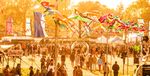 Festival-goers walking through the Shindig site beneath colourful fabric decorations in evening sunlight. Photograph by Dan Cadell.