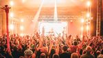 Crowd members raise their hands towards a brightly lit stage inside a marquee at Lindisfarne Festival.