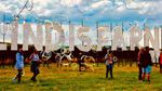 Soap bubbles drift across festival-goers standing in front of the large Lindisfarne sign.