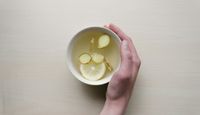 Hand holding a cup with ginger and lemon in hot water.