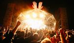 Large crowd raising their hands at a Greenbelt Festival main stage show at night, with bright golden lights and two large hand sculptures above the stage.