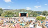 Green man festival in the sunshine! Festival goers relaxing in the sunshine in front of the main performance stage with the Brecon Beacons hills in the distance.