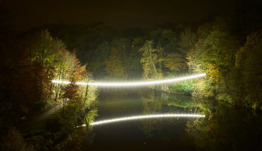 Beam of warm white light across a river illuminating reflection at the Lumiere Festival, Durham