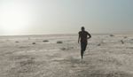 Film still showing a lone runner crossing a dry and open desert landscape.