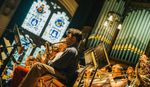 Big Band Jazz musicians performing in a church with pipe organ and stained glass window in the background.