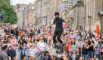 Street performer at Edinburgh Fringe Festival on an elevated unicycle with large crowd watching.