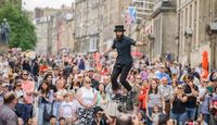 Street performer at Edinburgh Fringe Festival on an elevated unicycle with large crowd watching.