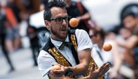 Man with shiny waistcoat juggling three oranges.