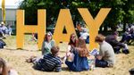 Festival-goers relax on the grass beside the large yellow Hay sign at Hay Festival. Photograph: Billie Charity / Hay Festival.