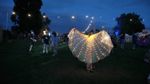 Festival goer displaying fairy-light cape against early evening background at Deer Shed festival.
