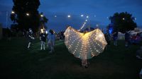 Festival goer displaying fairy-light cape against early evening background at Deer Shed festival.