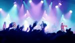 Image of the music stage at Cambridge Folk Festival, stage lights in pastel blues and pinks with crowd silhouette in the foreground.
