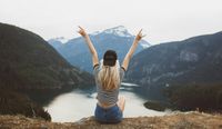 Woman looking out over nature scene with hands raised.