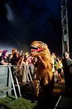 A person in an inflatable dinosaur costume greets audience members at the stage barrier during Dinosaur Pile-Up at 2000trees Festival. Photograph by Carla Mundy.