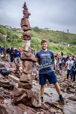 Denton Machuga standing beside a tall balanced stone tower at Bayswell Beach; photograph by James Craig Page.