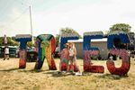 Two festivalgoers pose in front of the large colourful TREES letters at 2000trees Festival. Photograph by Carla Mundy.
