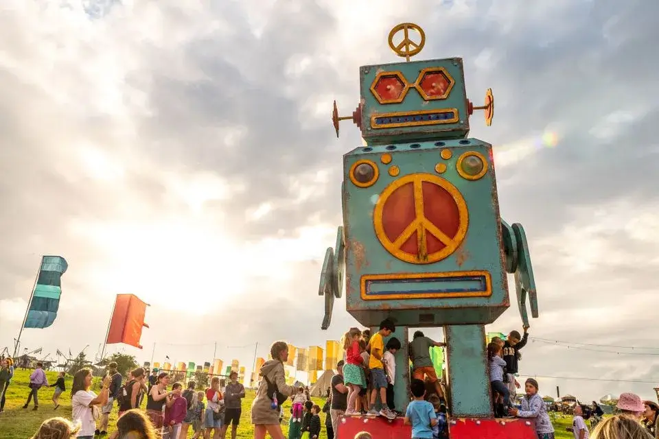 Famous peace robot from Camp Bestival with children climbing around the robot feet.